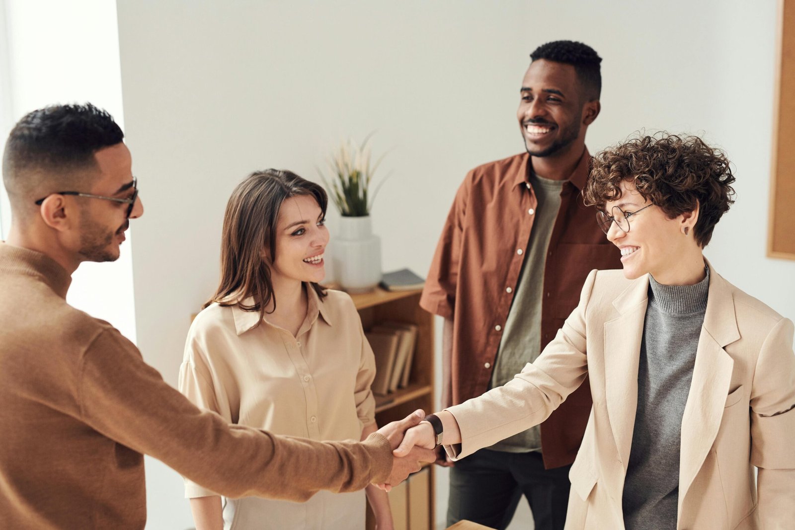 About Four colleagues smiling and shaking hands in a bright office setting.