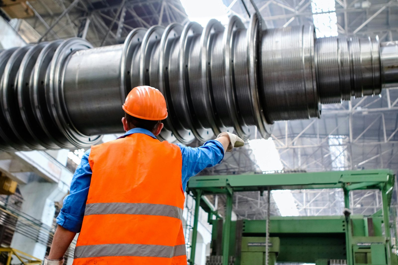 Services Engineer in high visibility vest and hard hat inspecting large machinery in factory setting.
